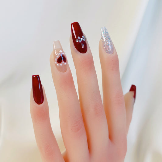 Close-up of a hand with red and clear nail designs on a light background