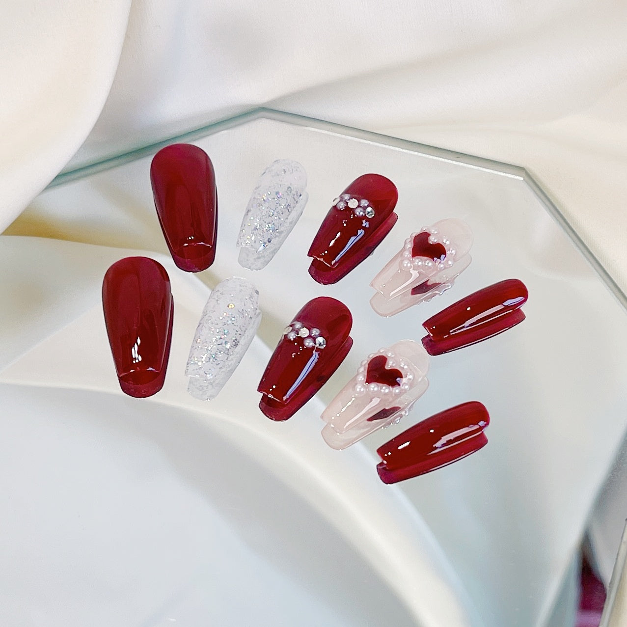 Set of red and beige nail designs with heart and glitter details on a white surface.